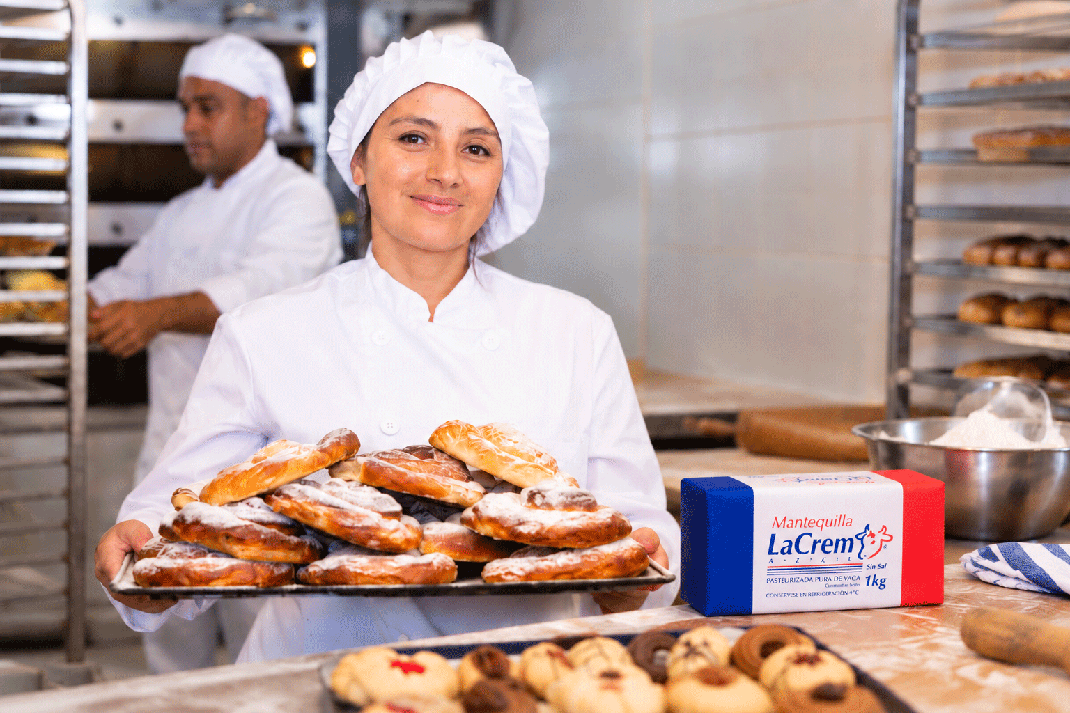Panadera con una charola de pan recién horneado junto a mantequilla La Crem